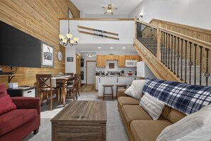 A cozy living room with a wooden floor, a red armchair, a brown sofa, and a wooden coffee table. - Cozy Mountain Condo with Resort Amenities | Pet-Friendly (Granby)