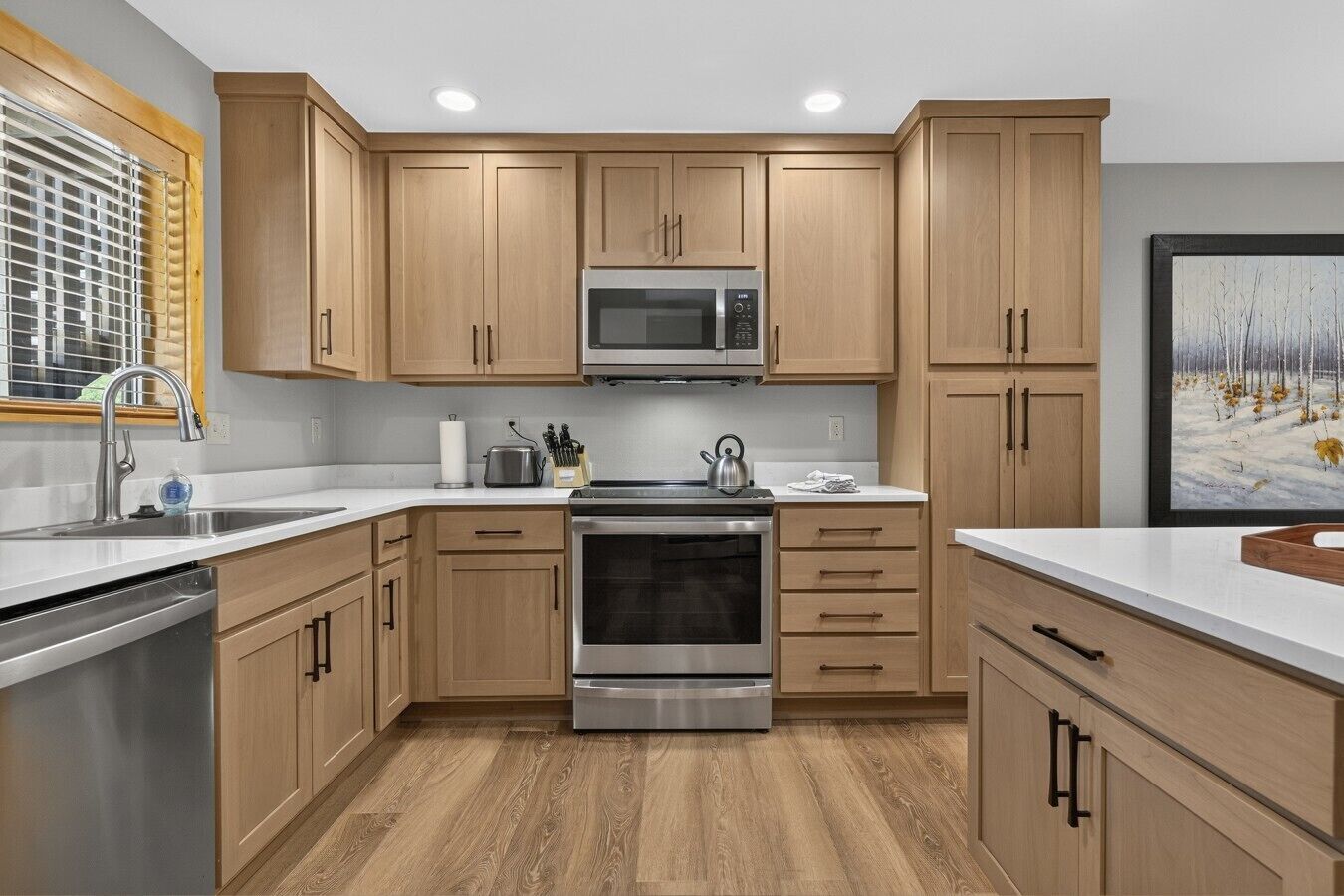 A modern kitchen with wooden cabinets, stainless steel appliances, and a window with blinds.