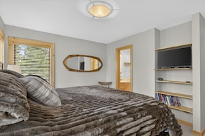 Ein Schlafzimmer mit einem Bett, einem an der Wand befestigten Fernseher und einem Fenster mit Jalousien.
