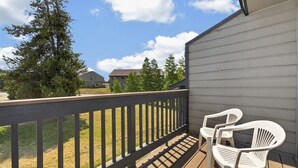 A balcony with a wooden railing, two white plastic chairs, and a view of a residential area with houses and trees. - Meadow Ridge Retreat | Pool, Hot Tub & Near Winter Park (Fraser)
