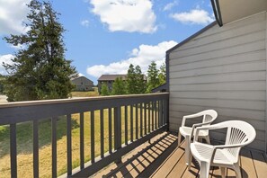 A balcony with a wooden railing, two white plastic chairs, and a view of a residential area with houses and trees. - Meadow Ridge Retreat | Pool, Hot Tub & Near Winter Park (Fraser)