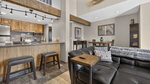 A modern kitchen with wooden cabinets, a bar area, and a dining space with a leather couch and a coffee table. - Meadow Ridge Retreat | Pool, Hot Tub & Near Winter Park (Fraser)