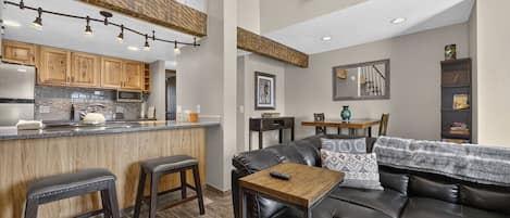Una cocina moderna con armarios de madera, una zona de bar y un espacio comedor con un sofá de cuero y una mesa de centro.