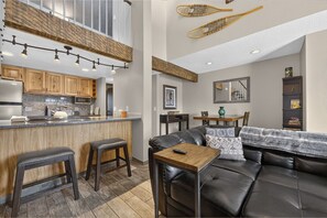 A modern kitchen with wooden cabinets, a bar area, and a dining space with a leather couch and a coffee table. - Meadow Ridge Retreat | Pool, Hot Tub & Near Winter Park (Fraser)