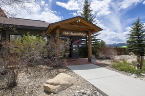 A lodge named Club Meadow Ridge with a wooden entrance, a flag, and a mountain view in the background. - Meadow Ridge Retreat | Pool, Hot Tub & Near Winter Park (Fraser)
