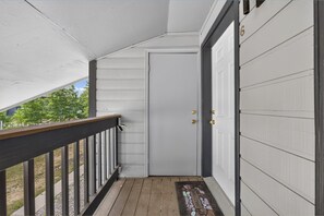 A covered porch with a wooden railing, a white door with a doorknob, and a welcome mat. - Meadow Ridge Retreat | Pool, Hot Tub & Near Winter Park (Fraser)