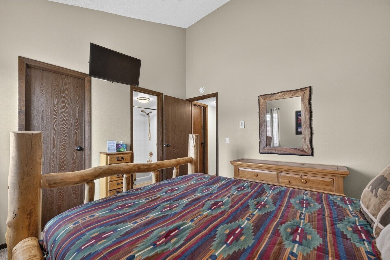 A bedroom with a bed, dresser, mirror, and wooden door.