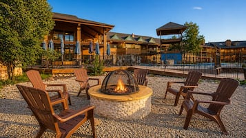 A fire pit with seating, a pool, and a building with multiple levels and outdoor seating.