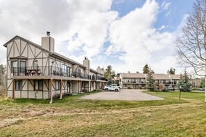Ein mehrgeschossiges Gebäude mit einem Balkon im Erdgeschoss, einem Parkplatz und einer Rasenfläche.