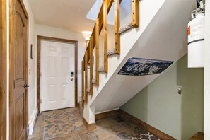 A hallway with a wooden door, a staircase with a white wall and a picture, and a fire extinguisher on the wall. - Cozy Fraser Retreat Near Winter Park Skiing (Fraser)