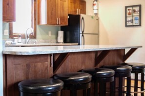 A kitchen with wooden cabinets, a black refrigerator, a countertop, and a bar stool area. - Cozy Fraser Retreat Near Winter Park Skiing (Fraser)