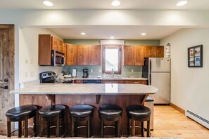 A modern kitchen with wooden cabinets, a central island with bar stools, and built-in appliances. - Cozy Fraser Retreat Near Winter Park Skiing (Fraser)