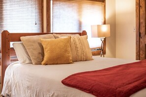 Ein Bett mit weißer Bettdecke, zwei beigen Kissen und einer roten Decke.