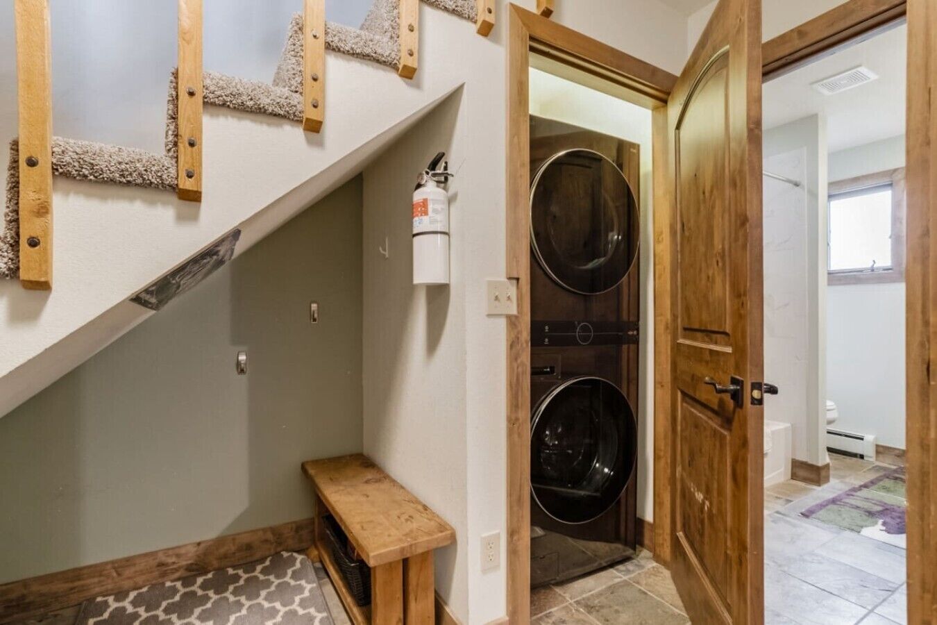 A laundry room with two large washing machines, a wooden bench, and a white wall-mounted fire extinguisher.