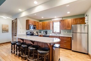 A modern kitchen with wooden cabinets, stainless steel appliances, and a central island with bar stools. - Cozy Fraser Retreat Near Winter Park Skiing (Fraser)