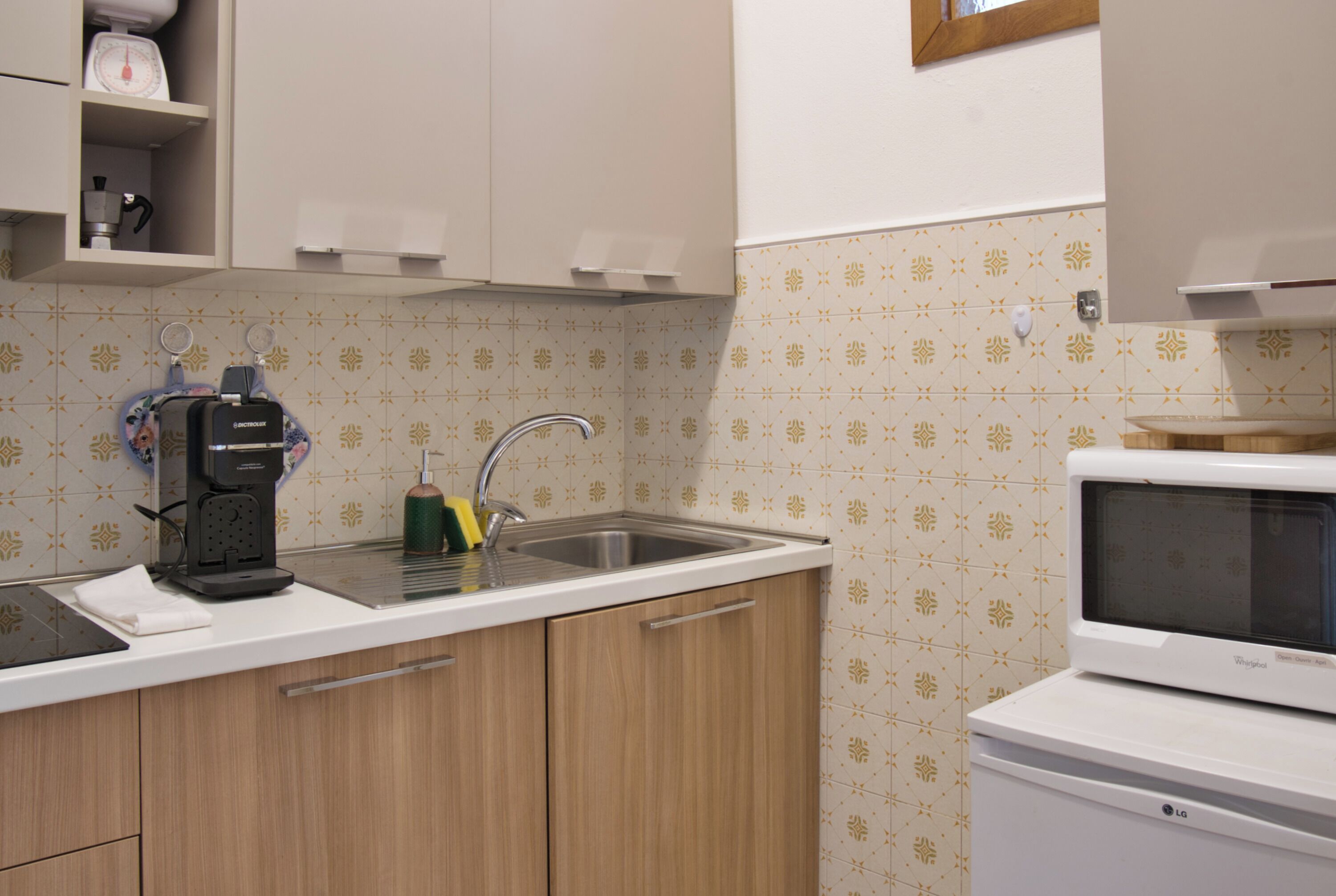 Una cocina con lavamanos, cafetera, microondas y azulejos decorativos en la salpicadera.