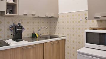 Una cocina con lavamanos, cafetera, microondas y azulejos decorativos en la salpicadera.