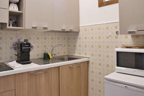 Una cocina con lavamanos, cafetera, microondas y azulejos decorativos en la salpicadera.