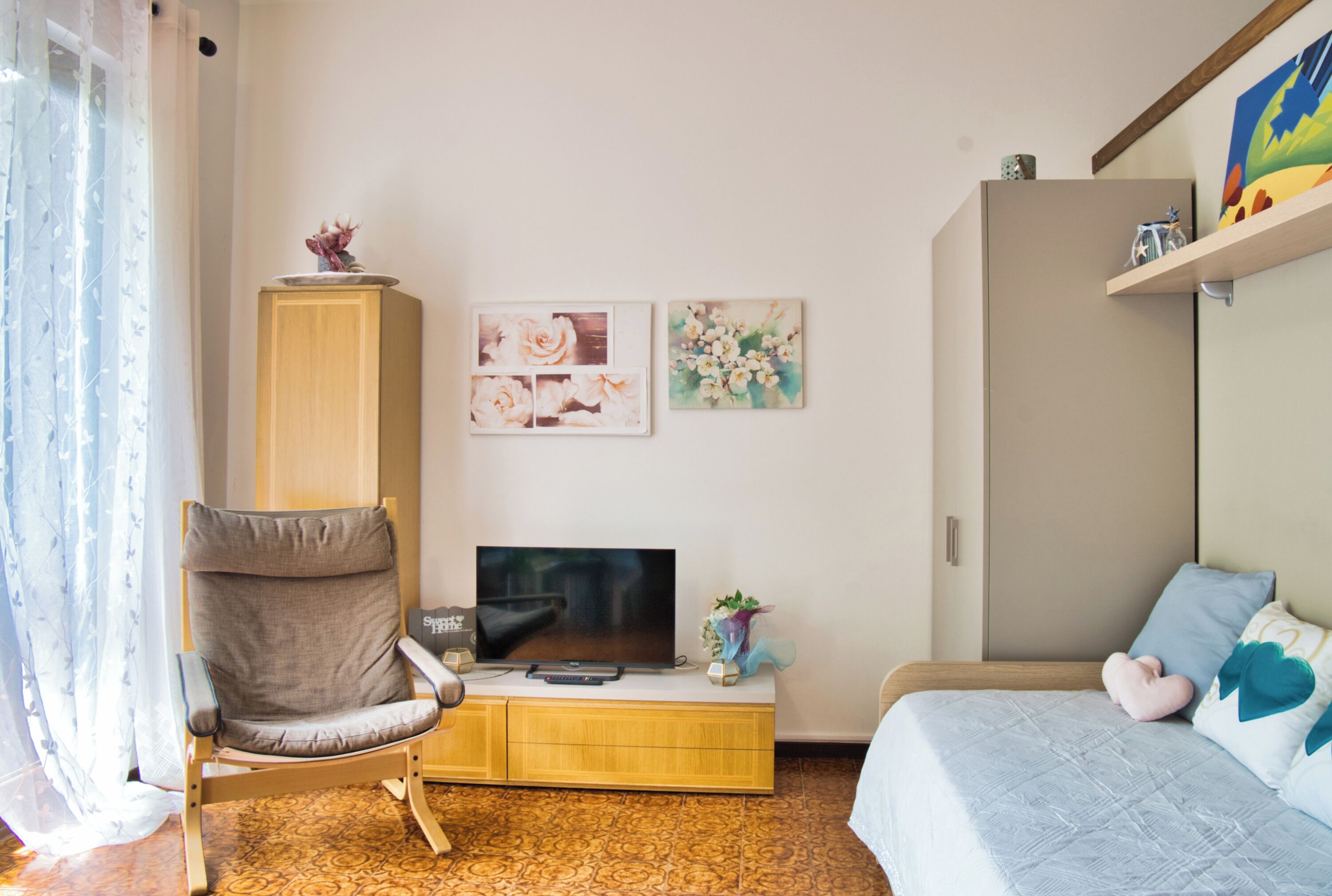 Een slaapkamer met een bed, een televisie, een kast en kunstwerken aan de muur.