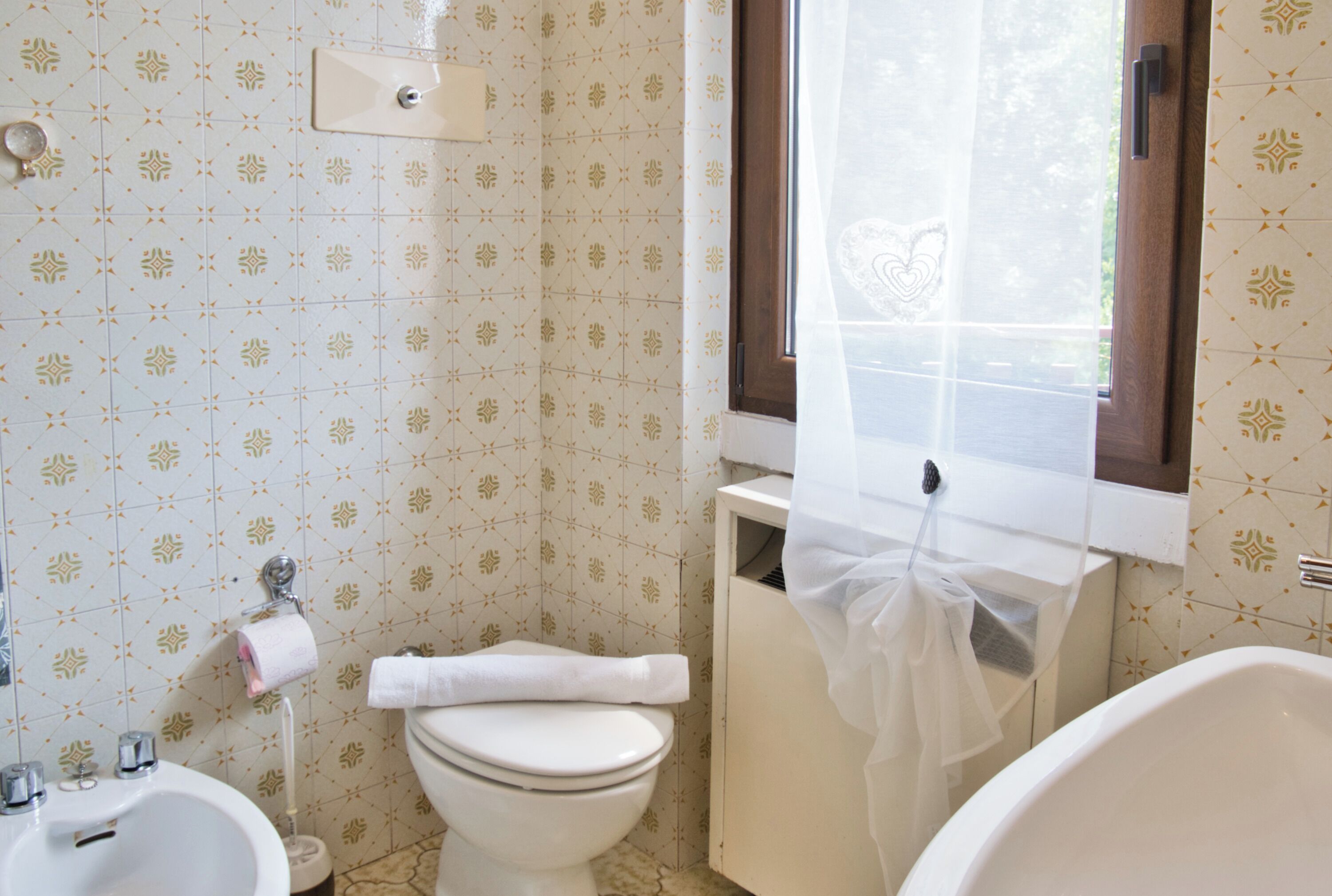 Un bagno con servizi igienici, bidet e vasca. C'è una finestra con tenda parzialmente tirata.