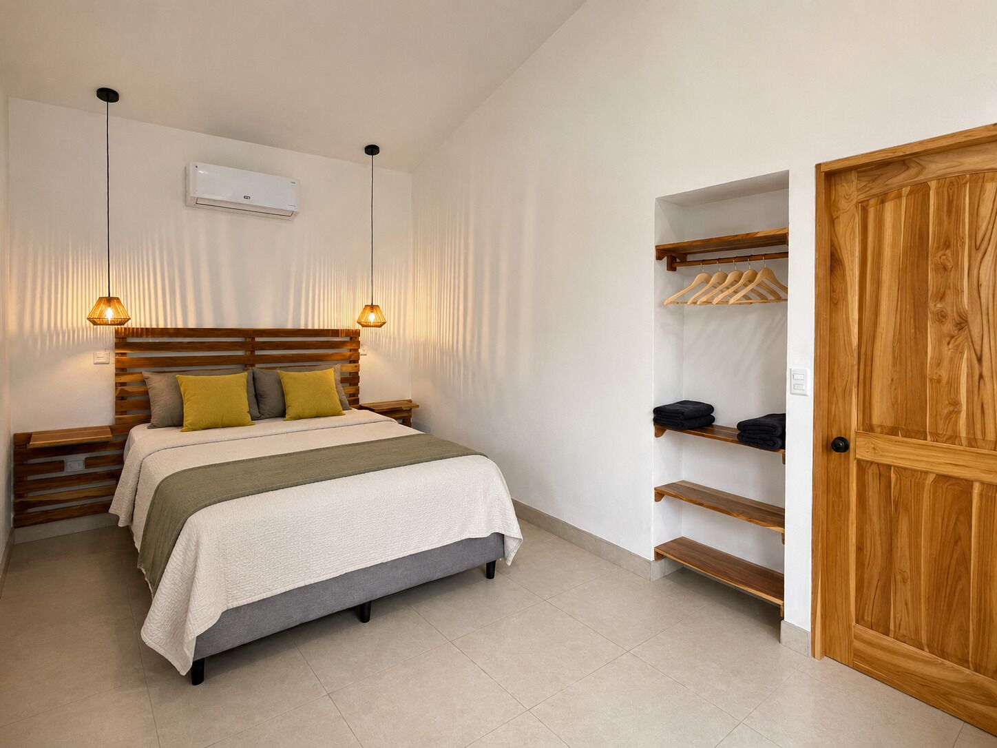 A bedroom with a bed, bedside tables, a hanging light fixture, a wardrobe with shelves, and a door.