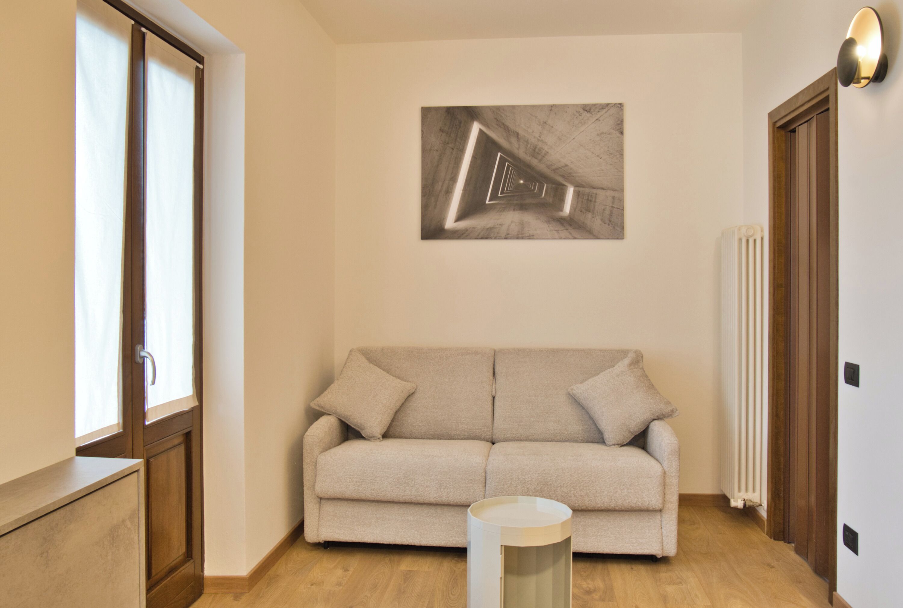 A room with a beige sofa, a painting on the wall, a radiator, and a wooden door.