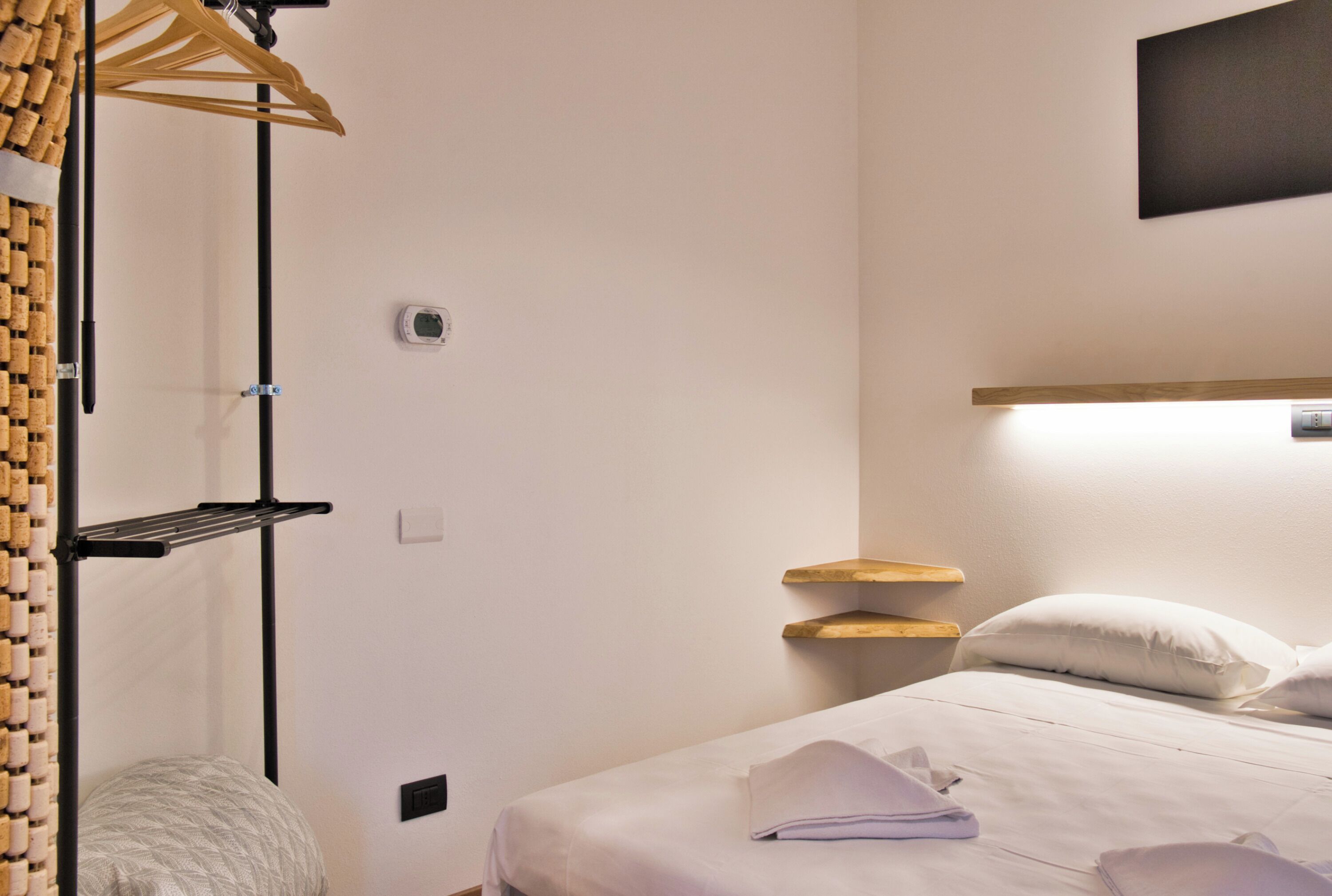 Une chambre d’hôtel comprenant un lit, une table de chevet, une étagère fixée au mur et un porte-manteau avec des bouchons de liège.
