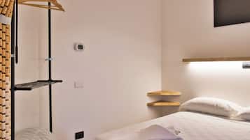 Une chambre d’hôtel comprenant un lit, une table de chevet, une étagère fixée au mur et un porte-manteau avec des bouchons de liège.