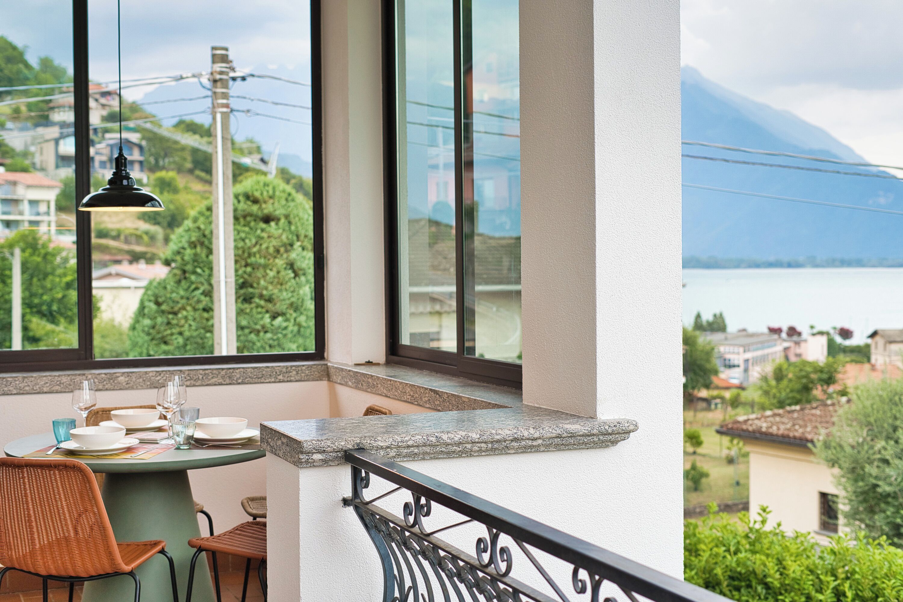 A balcony with a table set for dining, overlooking a scenic view of a lake and mountains.
