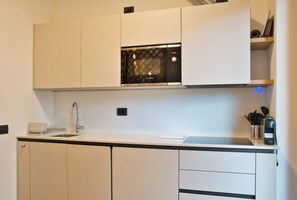 Una cocina moderna con armarios blancos, un microondas Bosch, un lavamanos y una encimera con cafetera y utensilios.