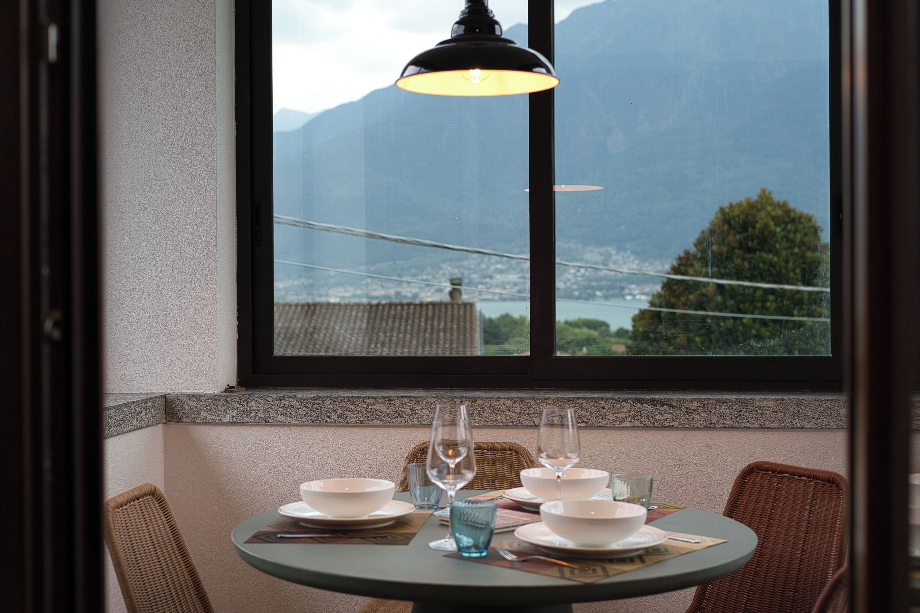 A dining table set with bowls, glasses, and a candle, overlooking a mountainous landscape through a window.