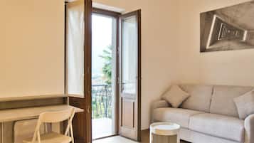 Une pièce comprenant un canapé, un fauteuil, une petite table et une porte donnant sur un balcon.
