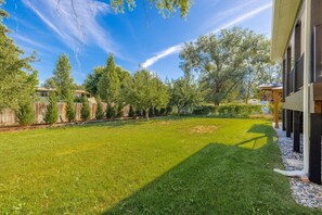 Ein Garten mit Rasen, Bäumen, einem Holzzaun und einem Gebäude mit Veranda.