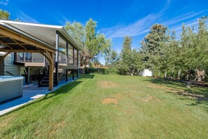 Ein modernes Haus mit überdachter Terrasse, einem gepflegten Rasen und ausladenden Bäumen.