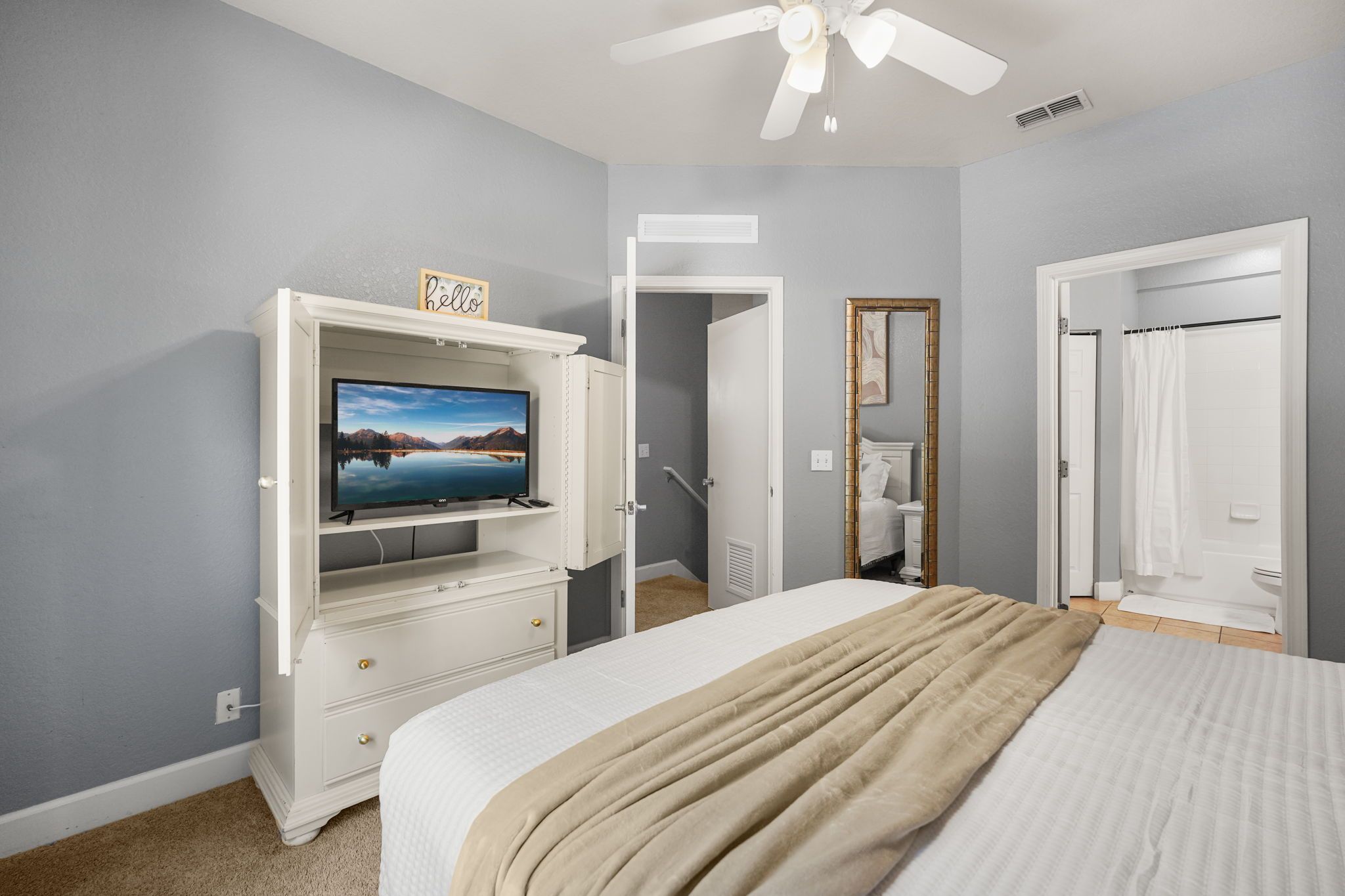 Une chambre à coucher avec un lit, un téléviseur posé sur une commode, un miroir et une porte donnant sur une salle de bain.