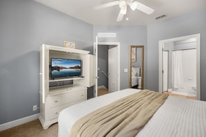 Ein Schlafzimmer mit einem Bett, einem Fernseher auf einer Kommode, einem Spiegel und einer Tür zu einem Badezimmer.
