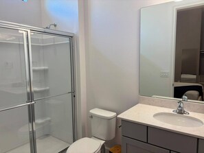 A bathroom with a glass shower enclosure, a toilet, a sink with a mirror above it, and a cabinet below. - 15 BD/ 16.5 BA/ Sonoma Resort (4231 SB) (Kissimmee)