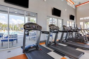 A gym with treadmills and exercise equipment, large windows, and a view of a pool and palm trees. - 15 BD/ 16.5 BA/ Sonoma (4231 SB) (Kissimmee)