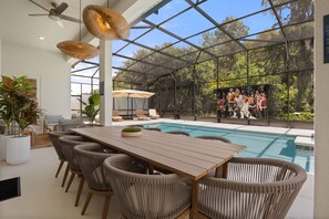 An outdoor pool area with a wooden table and wicker chairs, surrounded by glass walls and a view of a basketball game. - 15 BD/ 16.5 BA/ Sonoma Resort (4231 SB) (Kissimmee)