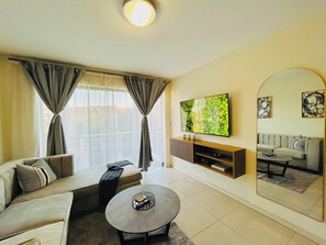 A modern living room with a sofa, coffee table, TV, and a large mirror. - Vue by LK Morningside (Sandton)