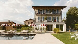Un edificio de dos pisos con piscina, mobiliario exterior y un césped cuidado.
