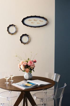 A dining area with a round table, clear chairs, a vase with flowers, and decorative plates on the wall.