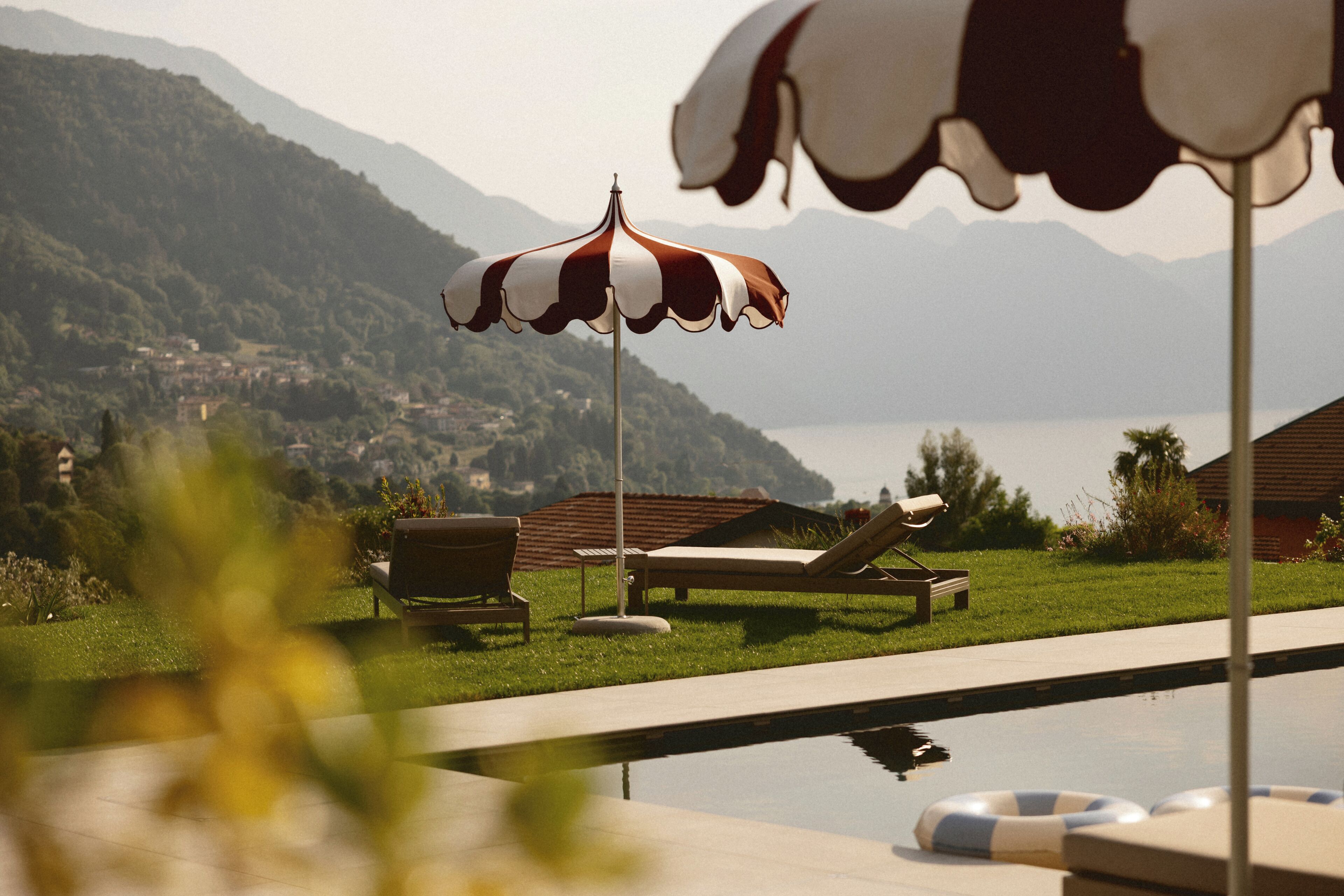 A pool area with lounge chairs and an umbrella, surrounded by a mountainous landscape.