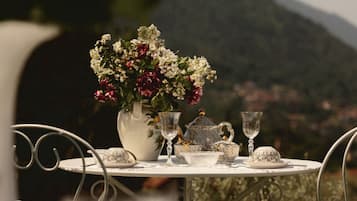 A table set with a vase of flowers, teacups, and a teapot, overlooking a mountainous landscape.