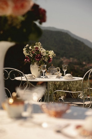 Une table dressée avec un vase de fleurs, des tasses à thé et une théière, donnant sur un paysage montagneux.