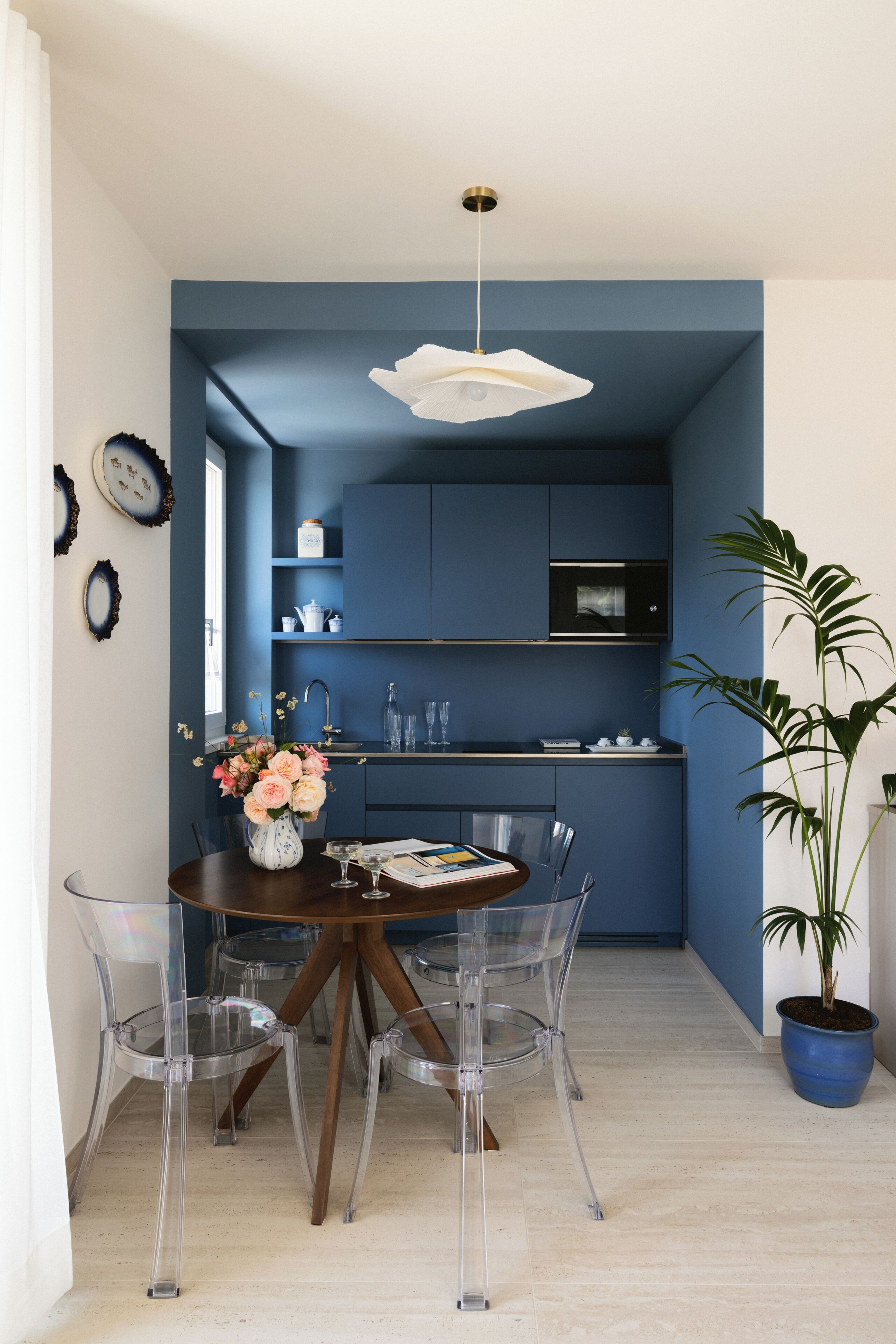 A modern kitchen with blue cabinets, a dining area with a round table and chairs, and a potted plant.