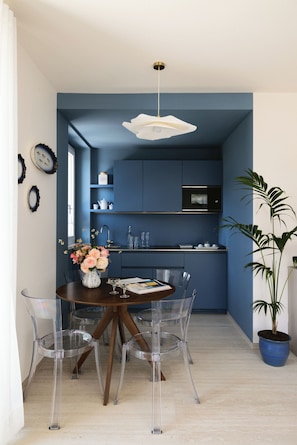 Une cuisine moderne avec des meubles de couleur bleue, un coin repas avec une table ronde et des chaises, et une plante en pot.