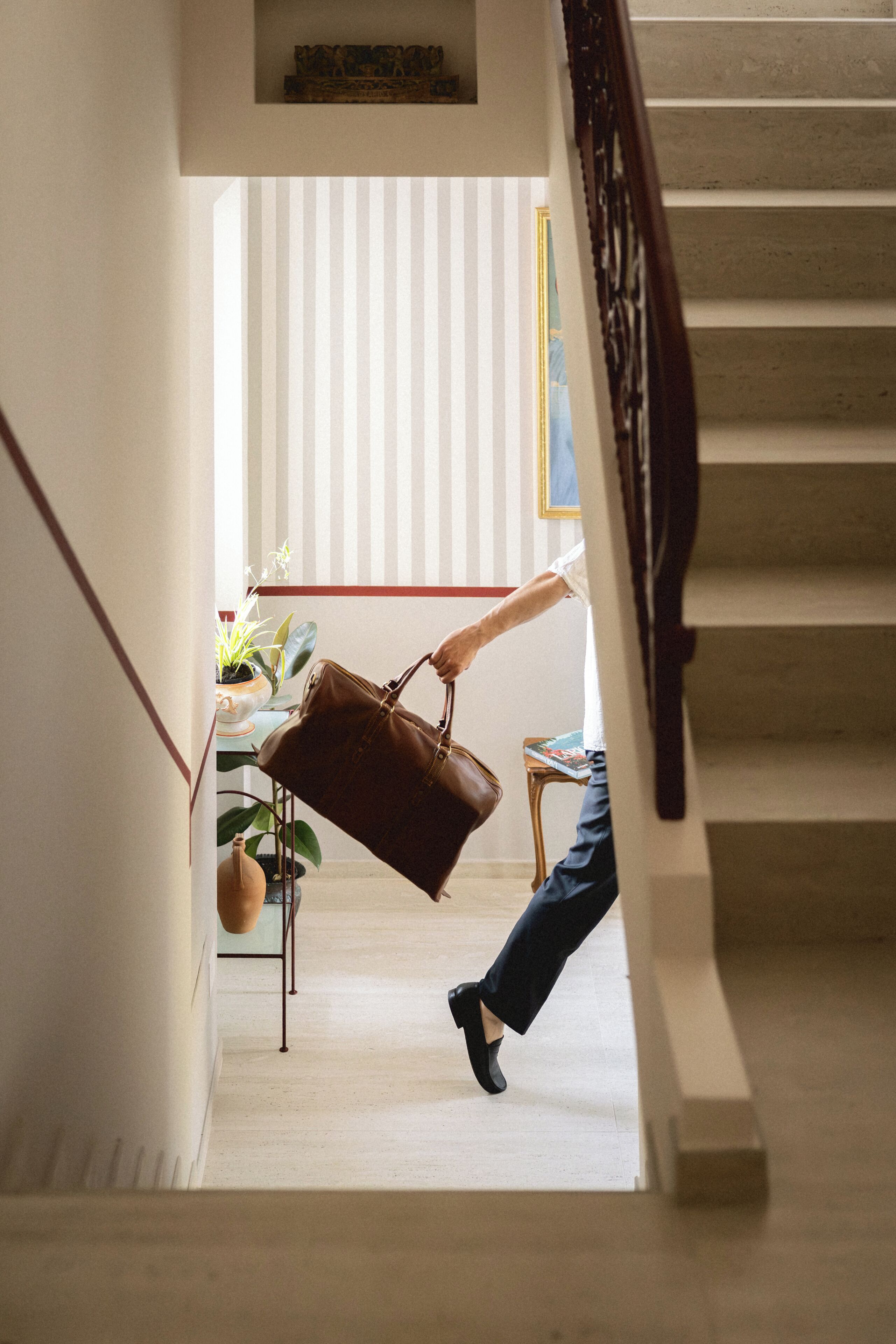 A staircase with a person descending, a brown leather bag, and a small table with a book.