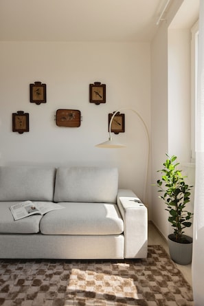A living room with a sofa, a floor lamp, a potted plant, and wall-mounted picture frames.