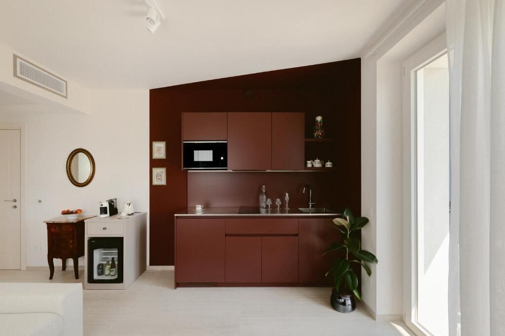 A compact kitchen with a microwave, sink, and cabinets. There is a small refrigerator and a potted plant.